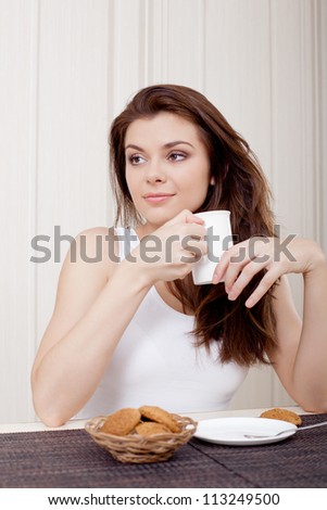 beautiful woman seated at her desk and enjoying tea and cookies, looking to the right