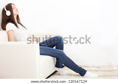 woman wearing white headphones sitting on sofa and listening to the music