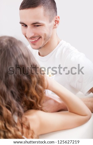 young couple sitting on the sofa eating popcorn and looking to each other, man laugh