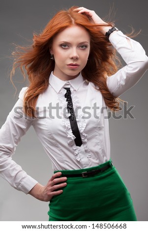 Redhead business woman in a green skirt on gray background looking to the side
