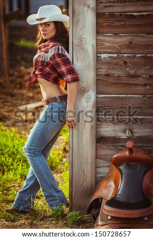 beautiful cowgirl style model posing with saddle on farmland