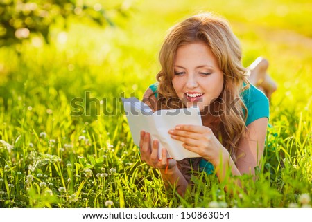 young blond woman reading a book lying on the grass in the shade