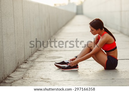 brunette runner woman sitting on the ground and tie laces, sunset time, evening workout