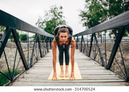 young slim woman doing yoga in the park on the wooden bridge