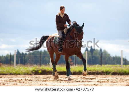 Horse riding: young girl riding on bay horse  in platz