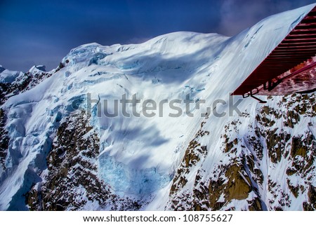 Aerial View of Cloud Bespeckled Blue Ice Snow Pack on Mountain Top in Alaskan Wilderness, Denali National Park, Alaska.  A Beautiful Snowscape of Rock, Snow, and Ice.  Red wing of our plane showing.