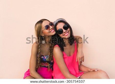 Closeup fashion lifestyle portrait of two pretty best friends girls,  wearing bright swag style floral hats, mirrored sunglasses, having fun and  make crazy funny faces. Two sisters posing on party. - Stock