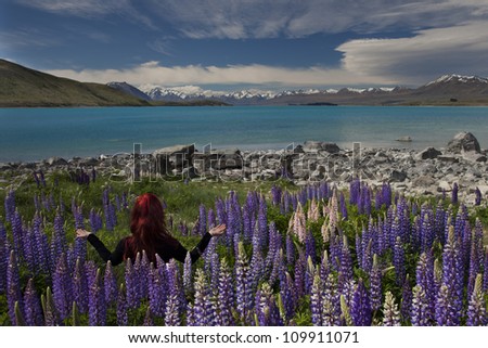 Red haired woman meditating in yoga position overlooking mountains, turquoise lake and flowers