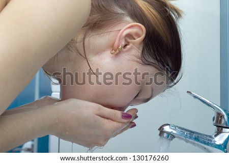 Woman washing face with water above bathroom sink