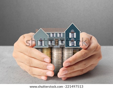 holding house representing home ownership and the Real Estate business holding house and coins
