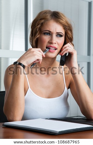 Beautiful woman concentrating using phone with pen in mouth
