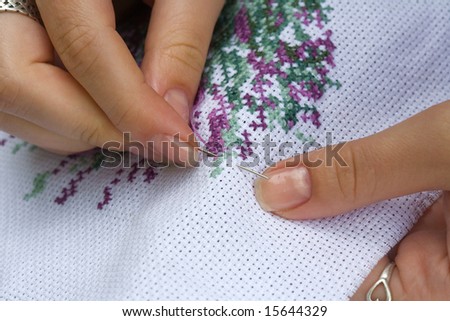 Fingers of young women, cross embroidery.