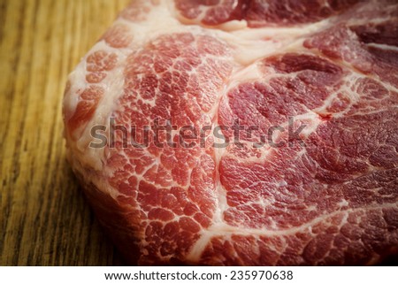 Piece of uncooked marbled steak or meat lying on a wooden counter in a kitchen or butchery, overhead view with copyspace