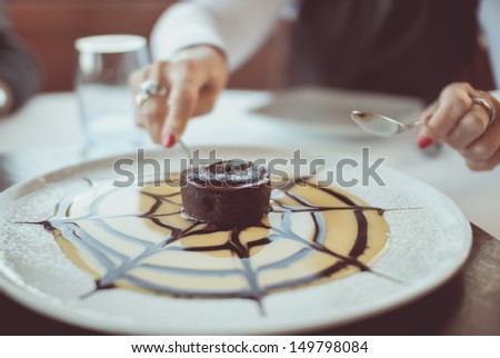 A photo of a woman\'s hands cutting a petit gateau small chocolate cake.