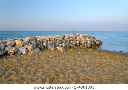 A beach boulder barrier wall in morning sun and a vibrant sea water in the background