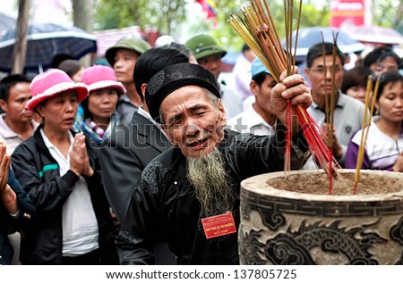 HANOI, VIETNAM - MARCH 30: A man places smoking incense sticks into an urn at the HUONG Temple on MARCH 30, 2013 in HANOI, VIETNAM . The incense is lit as an offering to the gods.