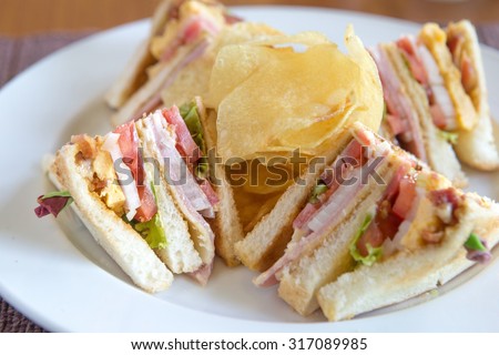 Photo of a club sandwich made with turkey, bacon, ham, tomato, cheese, lettuce, and garnished with a pickle and two cherry tomatoes.