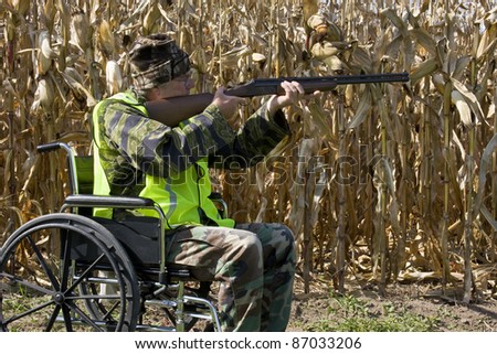 disabled hunter in a safety vest shooting a shotgun in a corn field