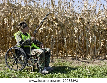 handicapped hunter in a wheelchair wearing a safety vest with a corn field in the background