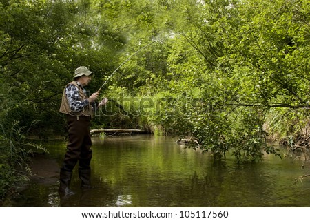 trout fisherman in a stream wearing waders and using a flyrod
