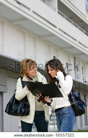 Real Estate woman Agent   with young woman customer standing  in front  of a new building and looking a document
