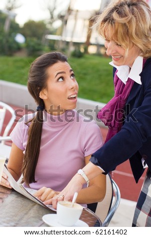 Young  female tourist sitting in Cafe and  asking  female mature passerby  about direction.