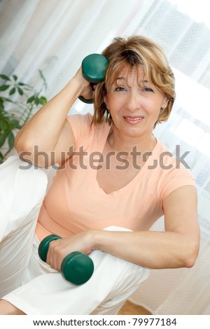 Tired Mature woman sitting on the floor after exercising with dumbbells at home.