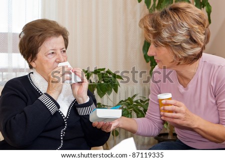 Serious senior woman blowing nose with handkerchief while a nurse giving to her the medicine.