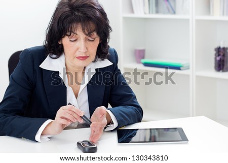 Mature businesswoman Checking Her Blood Sugar Level  in the office. Shallow dof.