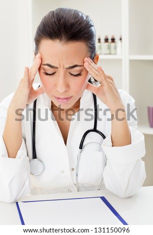 Female doctor  with closed eyes sitting at the table and  holding her  head in hands.
