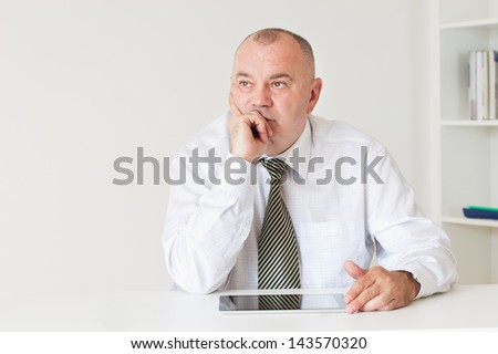 Mature businessman sitting at the table with hand on his chin and looking away.