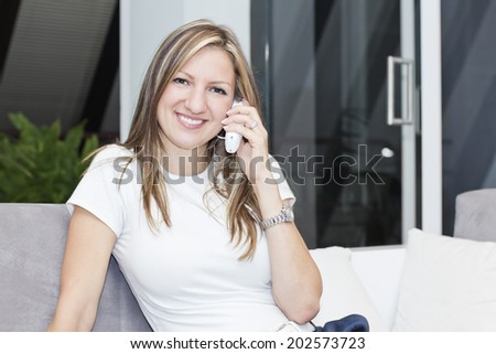 Charming woman sitting on the sofa and chatting  by phone  with friends.