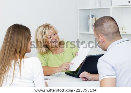 Mature female consultant showing  a document to young couple clients.