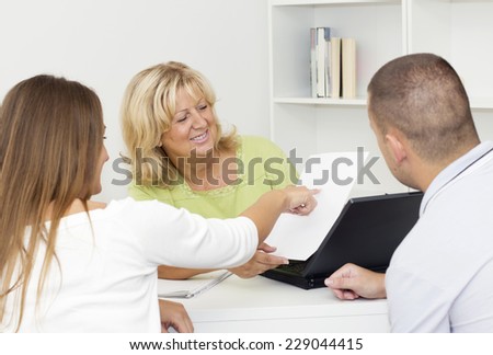 Mature female consultant showing  a document to young couple clients.