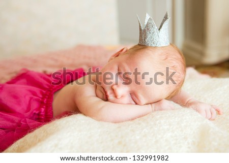 A newborn baby is wearing in a princess costume and sleeping on a soft white background. Childhood or parenting concept.