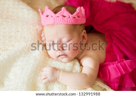 A newborn baby is wearing in a princess costume and sleeping on a soft white background. Childhood or parenting concept.