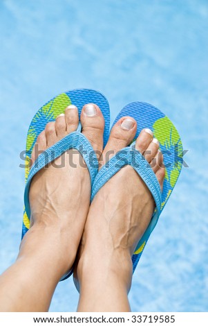 Woman\'s Feet Wearing Flip Flops Over a Swimming Pool