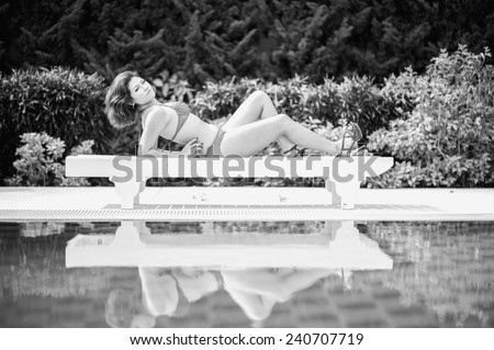 black and white bikini asian woman on sunbathing lounge by the pool
