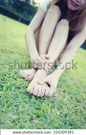relaxation concept, relaxed young woman with bare feet sitting on grass, focus foot