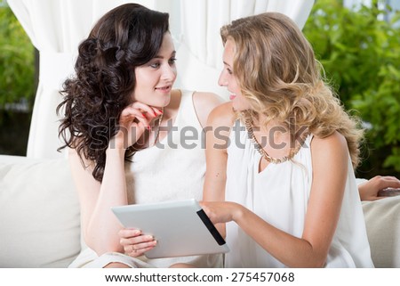 Best friends - young women sitting in a cafe with tablet pc and talking to each other.