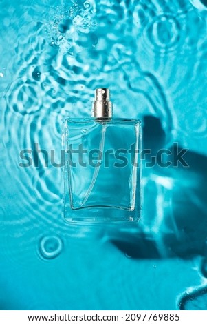 Transparent bottle of perfume on a blue water background. Fragrance presentation with daylight. Trending concept in natural materials with beauty shadow. Women's and men's essence.