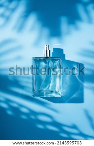 Transparent bottle of perfume on a blue background. Fragrance presentation with daylight. Trending concept with beautiful shadows. Women's essence.