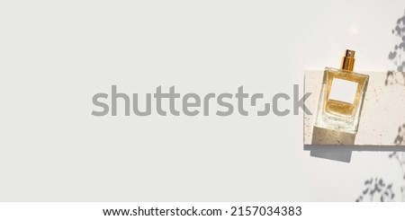 Transparent bottle of perfume with white label on stone plate on a white background. Fragrance presentation with daylight. Trending concept in natural materials with plant. Women's and men's essence.