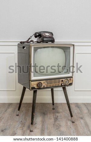Old Television with 4 legs in the corner of vintage room and a black old telephone on it