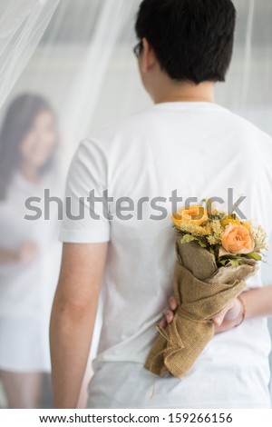 Asian guy holding flower behind him trying to surprise his waiting girl friend