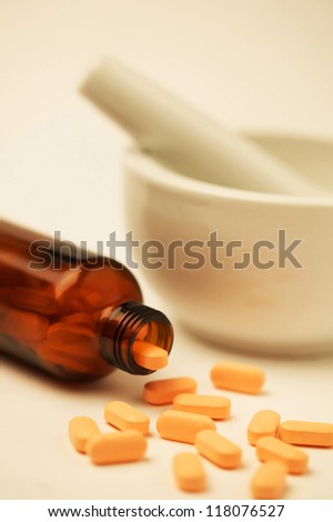 A bowl, a medicine pestle, a brown bottle and orange tablets