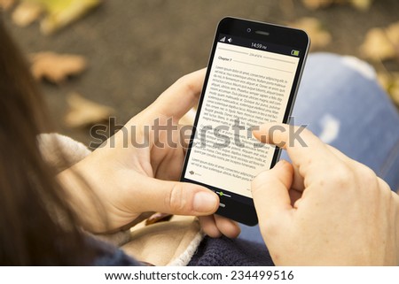 technology and lifestyle concept: young woman reading a book on a phone screen at the park