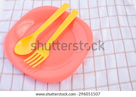 yellow fork and spoon, pink plastic plate on tablecloth background