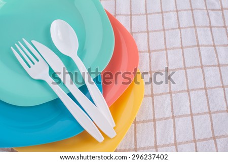 white fork ,knife and spoon put on colorful plastic plate at tablecloth
