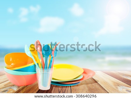Colorful Plastic tableware picnic set on wooden plank table with summer sea and blue sky blurred background